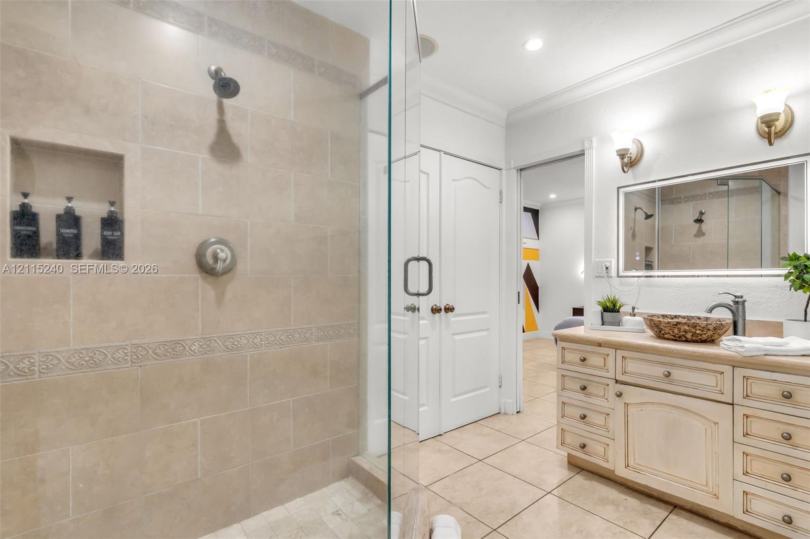 Walk-in shower featuring floor-to-ceiling tile, a built-in recessed storage niche, and a glass enclosure, paired with a custom vanity cabinet and framed vanity mirror