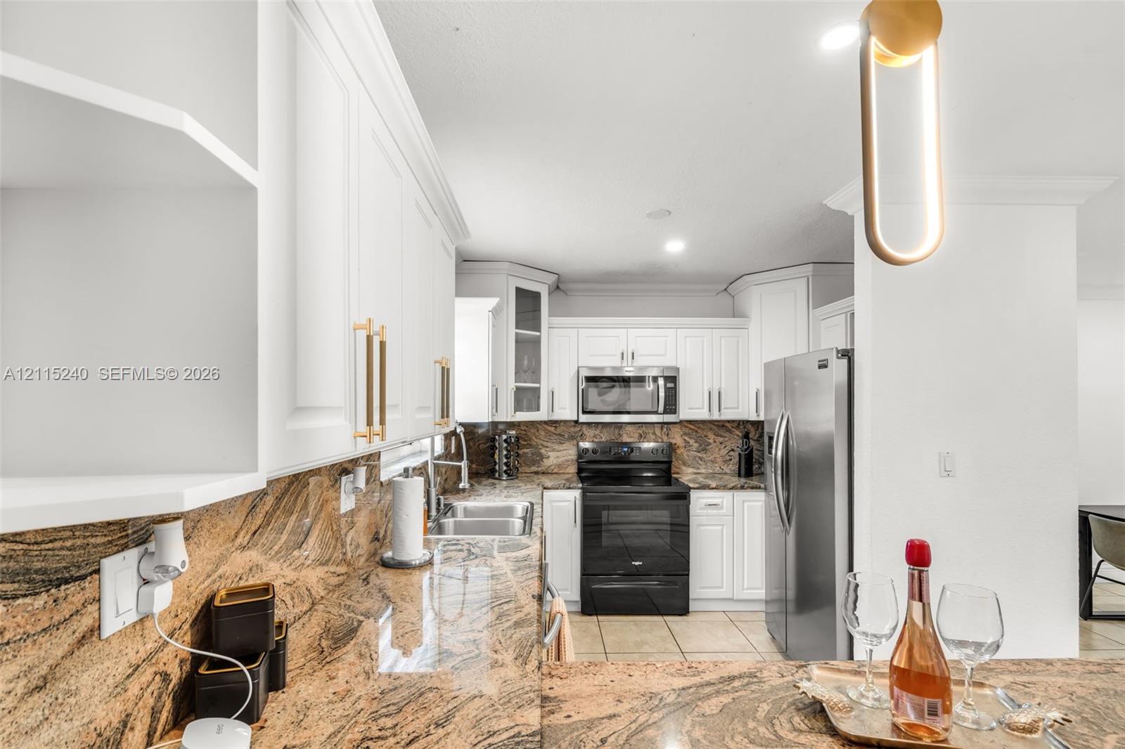 Kitchen featuring white cabinetry with gold-tone hardware, stone countertops, stainless steel appliances, and contemporary pendant lighting