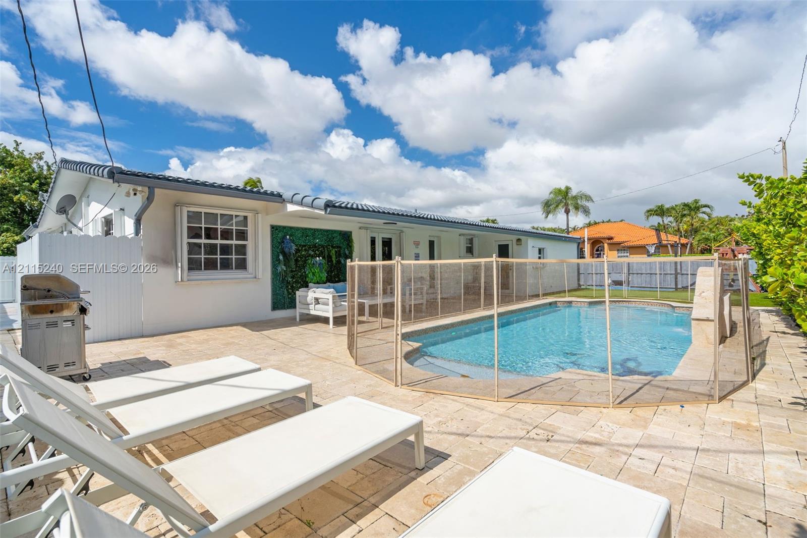 Outdoor space featuring stone-paver decking, a swimming pool with a stone waterfall feature, and a privacy fence