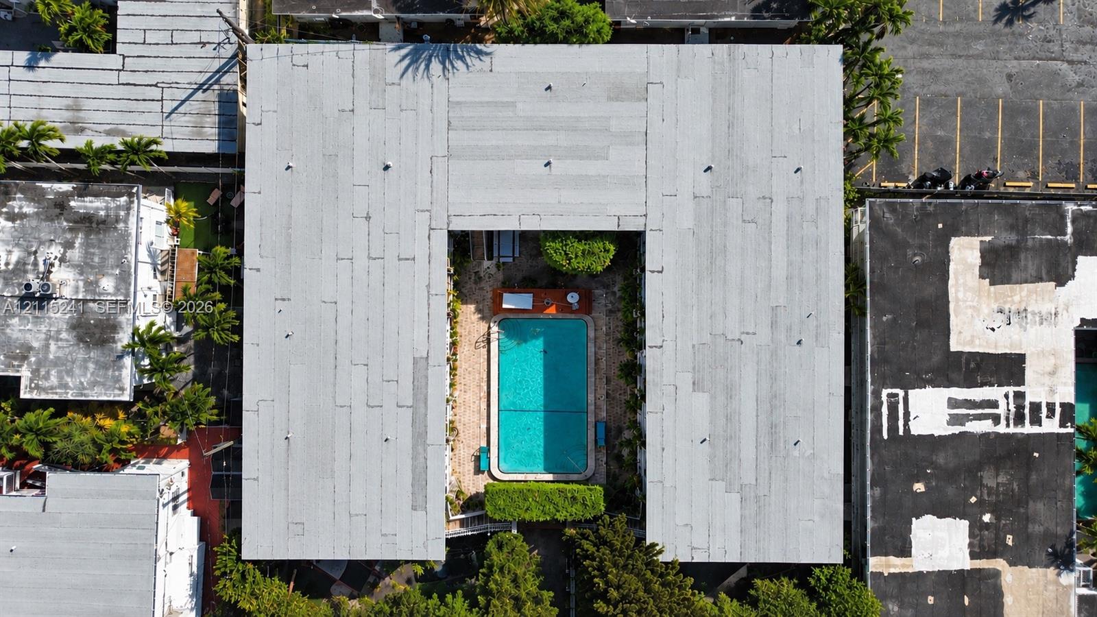 Aerial view of a U-shaped building featuring a central courtyard with a swimming pool, paved surface, and manicured landscaping