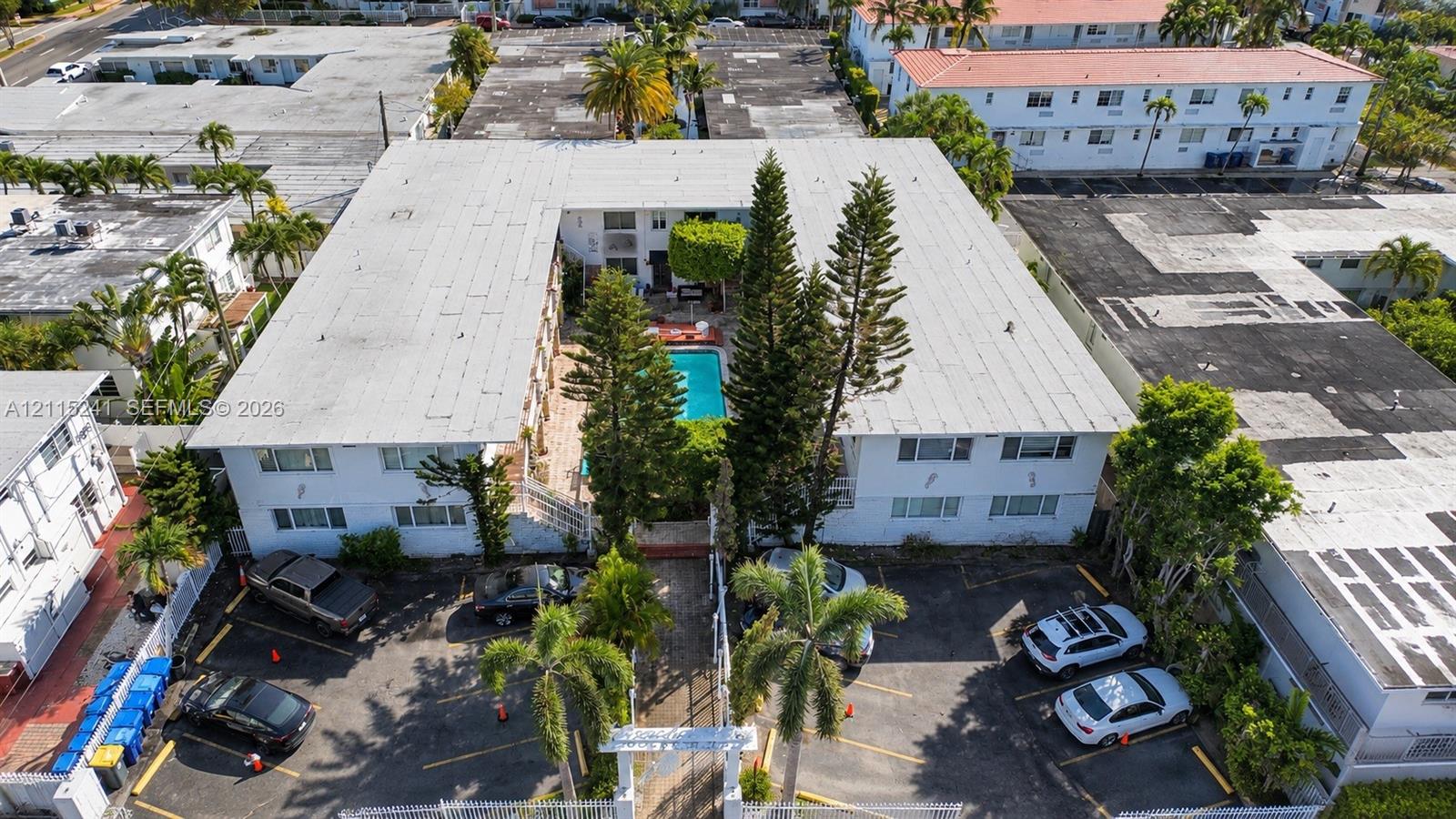 U-shaped multi-unit building featuring a central courtyard with an in-ground swimming pool, mature perimeter landscaping, and dedicated surface parking