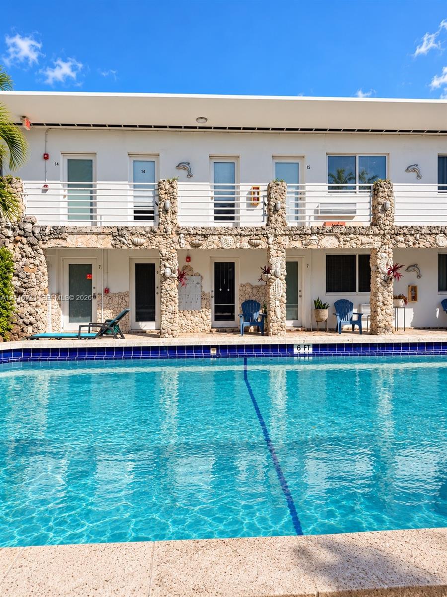 Swimming pool with blue tile edging and stone-textured coping, featuring a two-story exterior facade with stone pillars and horizontal metal railing
