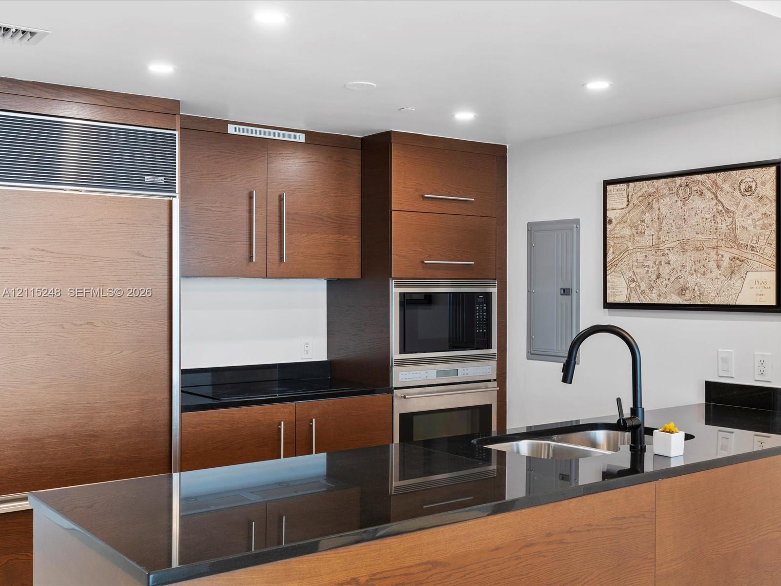 Kitchen featuring wood cabinetry, integrated panel-front refrigerator, dark solid-surface countertops, stainless steel wall oven and microwave, and a black gooseneck faucet