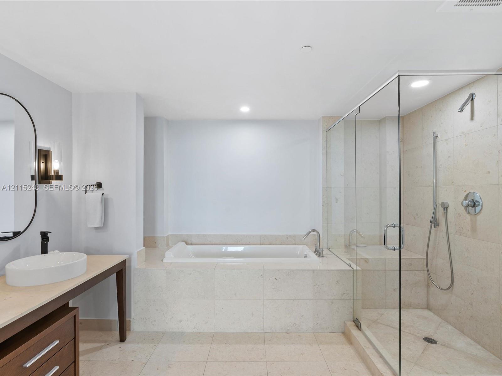 Bathroom featuring a stone-tile surround soaking tub, a frameless glass-enclosed shower with handheld fixture, stone-tile flooring, and a floating vanity with a vessel sink