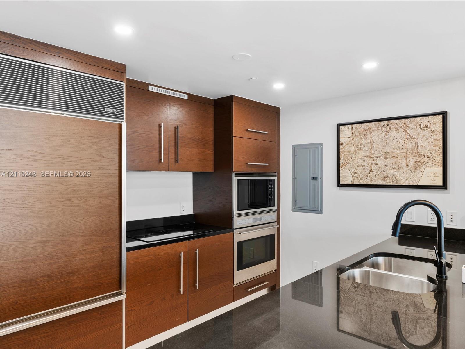 Kitchen featuring dark wood-finish cabinetry, built-in stainless steel double wall ovens, panel-ready refrigerator, polished stone countertops, and a matte black gooseneck faucet