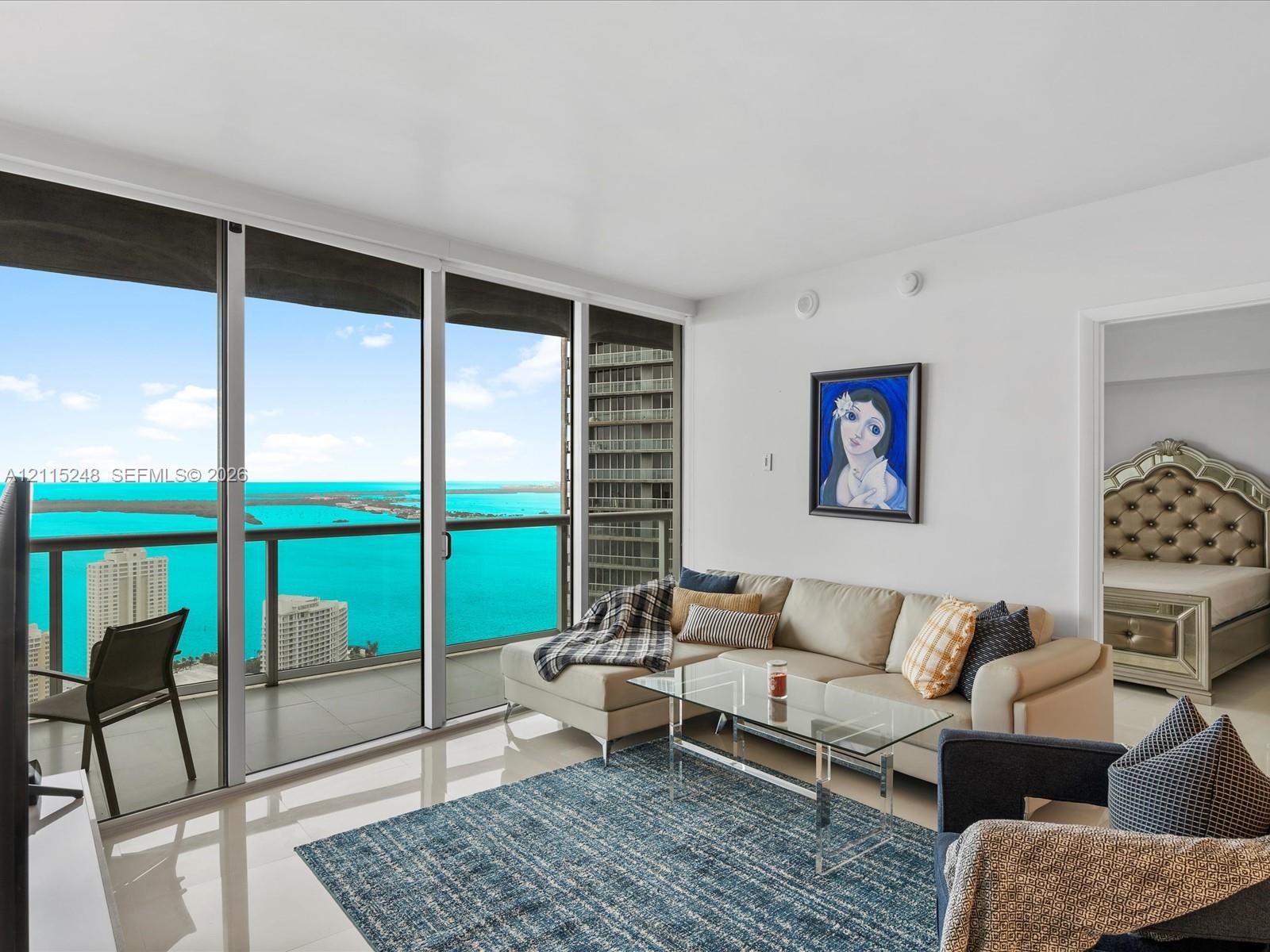 Floor-to-ceiling sliding glass panels, balcony with metal railing, polished neutral-toned flooring, and expansive water scenery