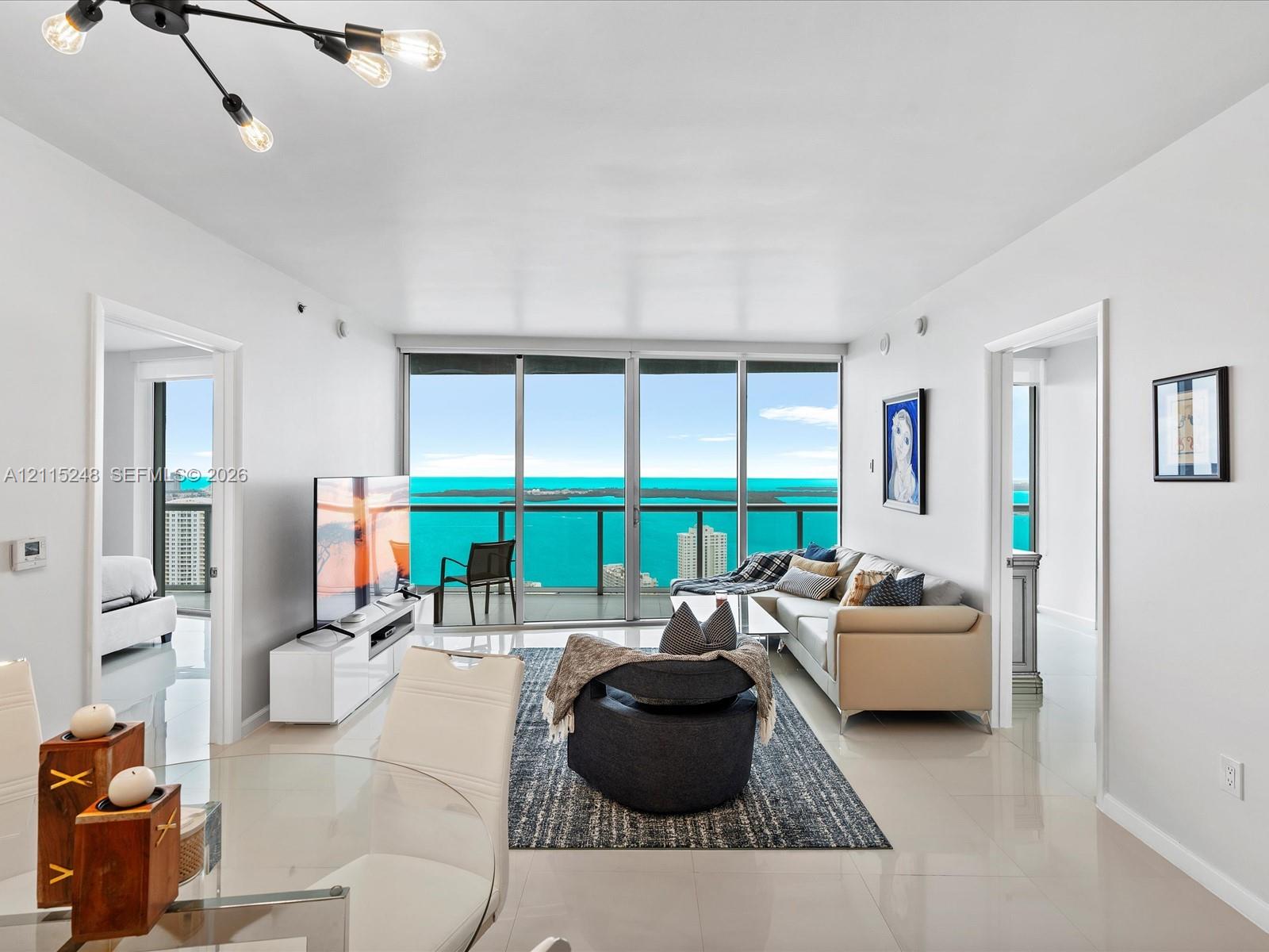 Living area featuring floor-to-ceiling glass sliding doors, a glass-railed balcony, large-format tile flooring, and multi-arm chandelier lighting