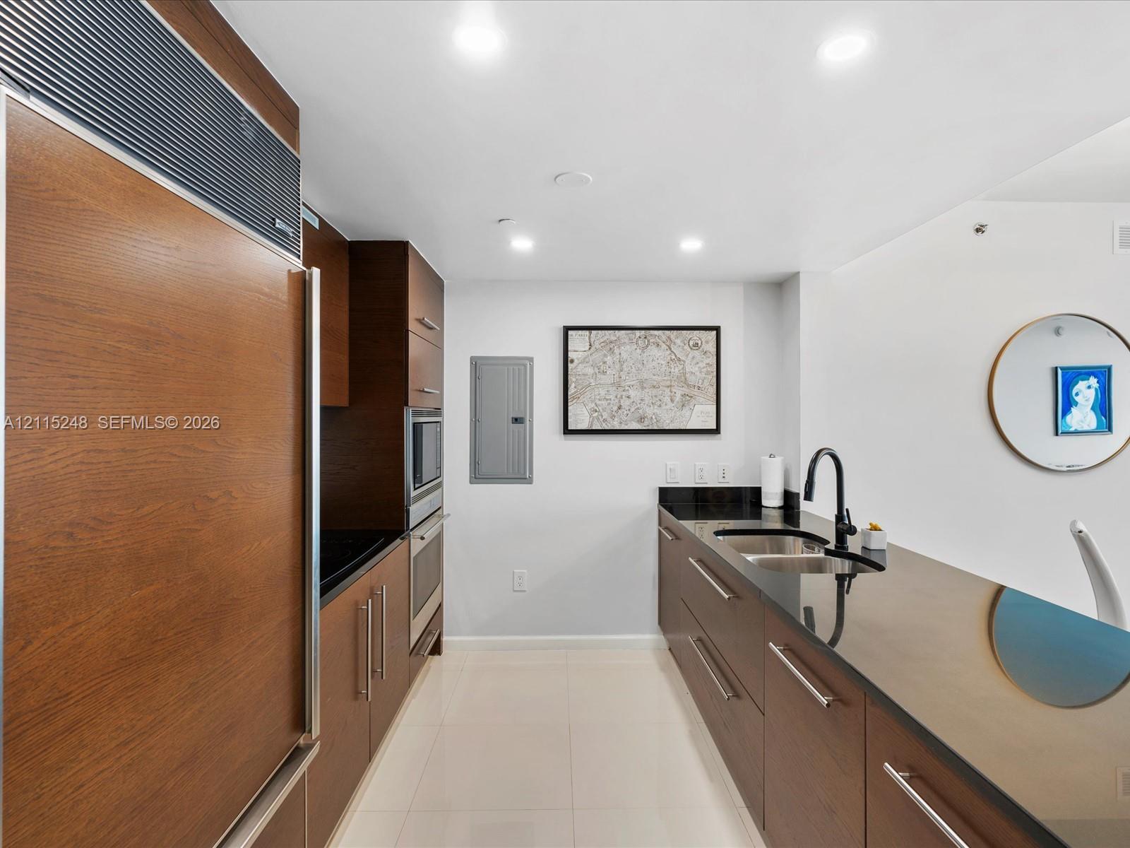 Kitchen featuring wood-finish cabinetry, built-in stainless steel appliances, dark stone countertops, undermount sink with a matte black faucet, and recessed ceiling lighting