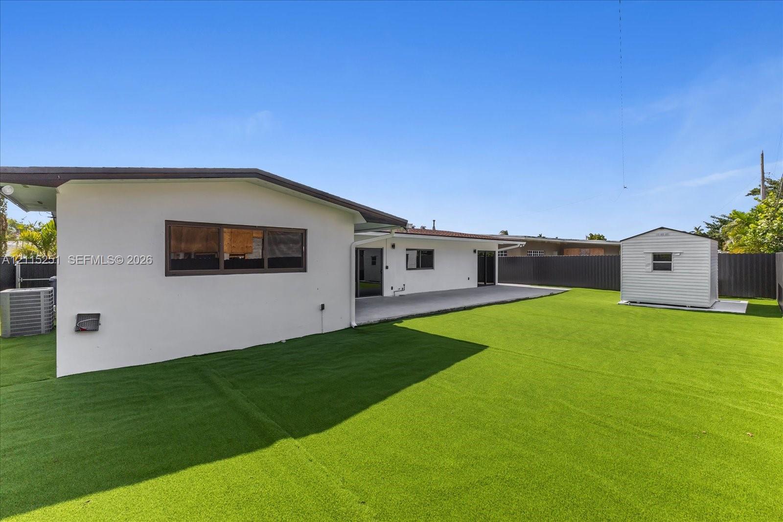 Backyard featuring low-maintenance synthetic turf, a concrete patio, perimeter privacy fencing, and a detached storage shed