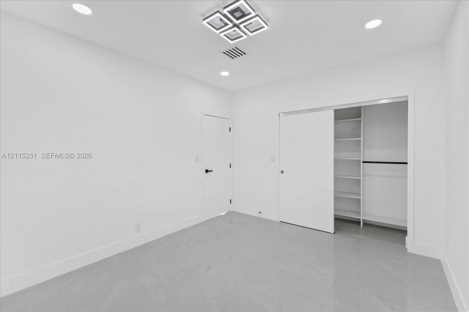 Bright room featuring polished tile flooring, recessed lighting, a modern geometric ceiling fixture, and a sliding closet door with integrated shelving