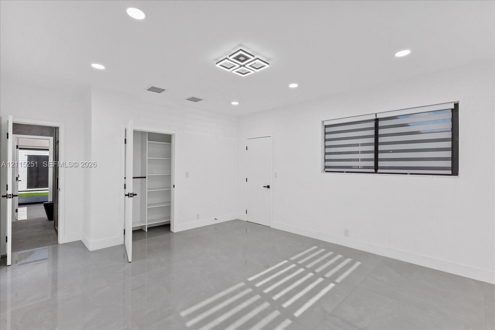 Interior space featuring large-format tile flooring, recessed ceiling lighting, a tiered geometric light fixture, and a built-in closet with integrated shelving