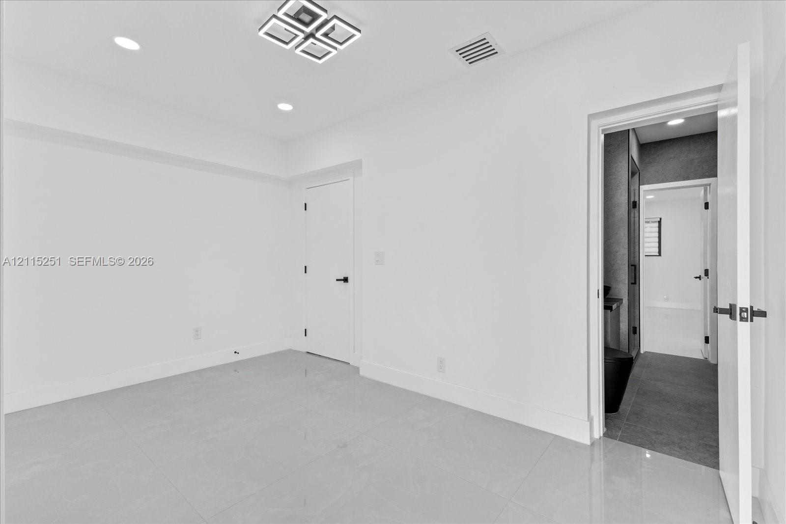 Interior room featuring large-format tile flooring, recessed lighting, and a geometric flush-mount ceiling fixture with matte black door hardware