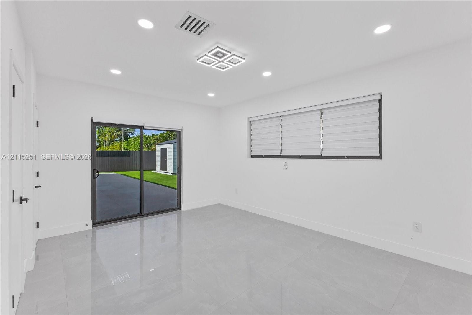 Neutral-toned tile flooring, recessed ceiling lighting, modern geometric flush-mount light fixture, and sliding glass door with horizontal window blinds