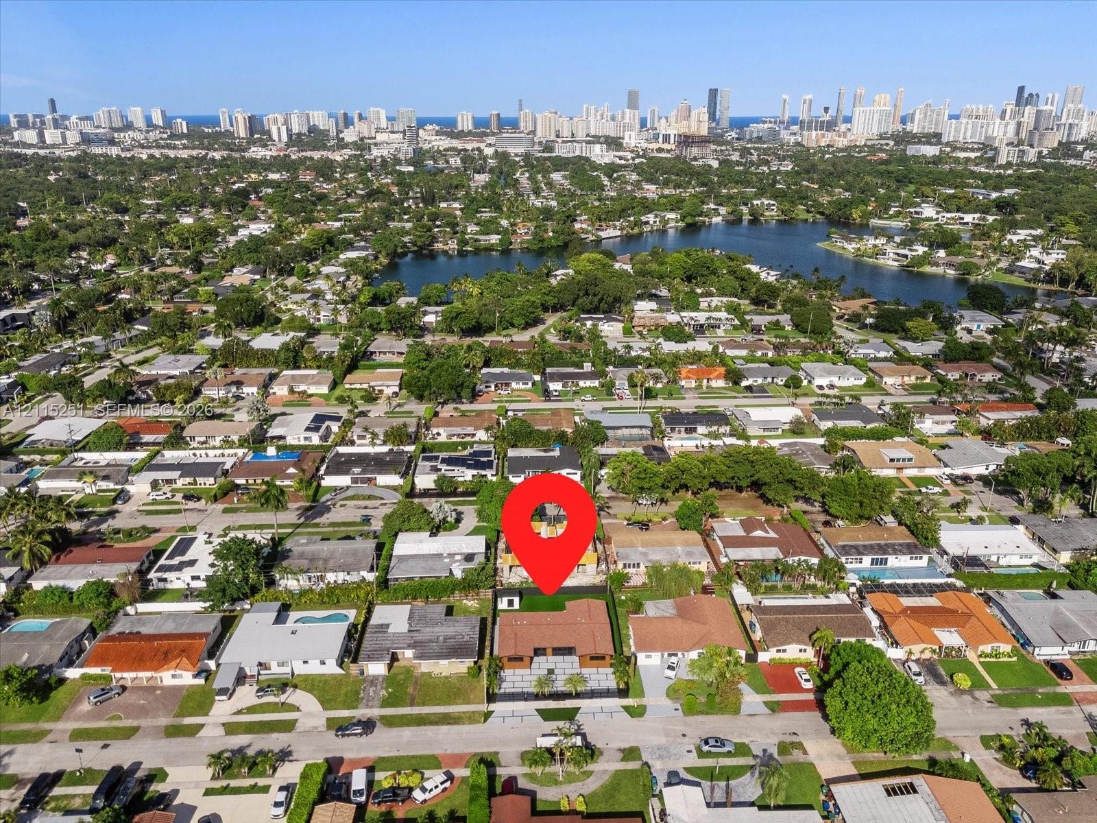 Aerial perspective showcasing a residential property with a paved driveway, rectangular roofline, and rear outdoor space including a swimming pool, all set within a coastal urban environment