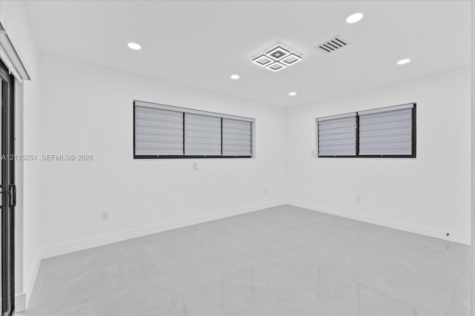 Neutral-toned large-format tile flooring, recessed ceiling lighting, square geometric flush-mount light fixture, and windows with black frames
