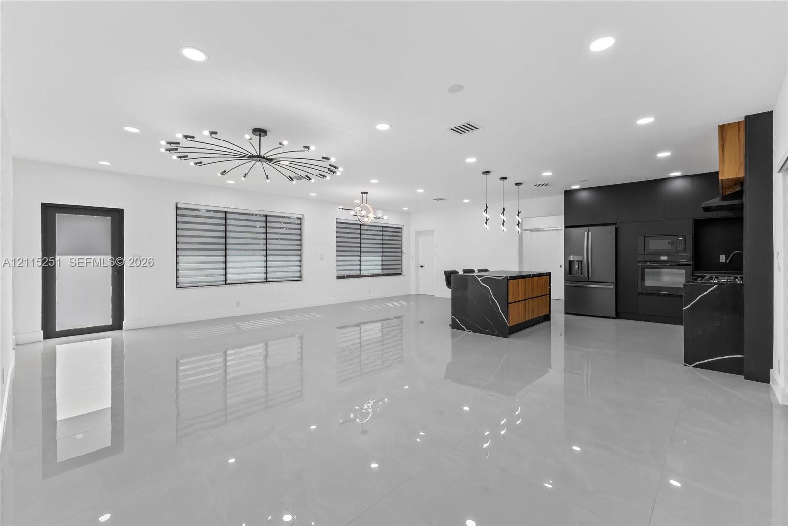Open-concept interior featuring large-format tile flooring, recessed lighting, a modern sputnik-style chandelier, and a kitchen equipped with flat-panel cabinetry and a waterfall-edge island