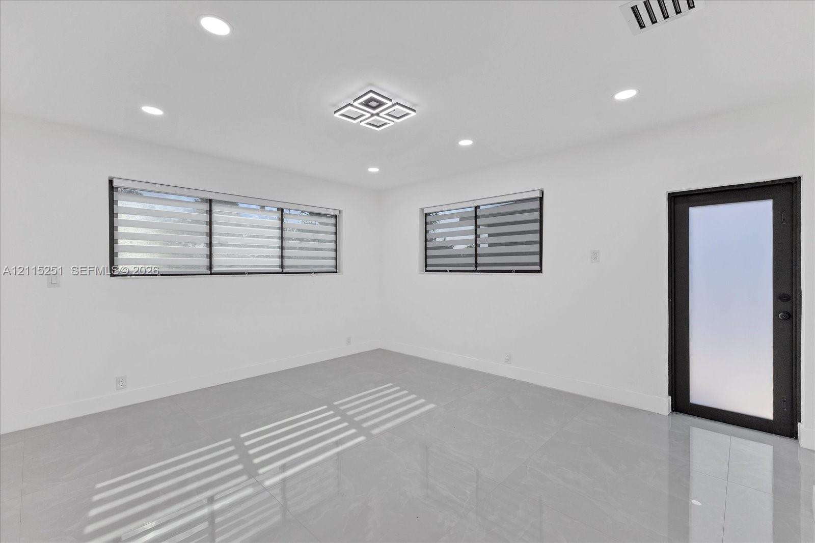 Interior space featuring polished porcelain tile flooring, recessed lighting, a modern geometric flush-mount light fixture, and an exterior door with frosted glass paneling