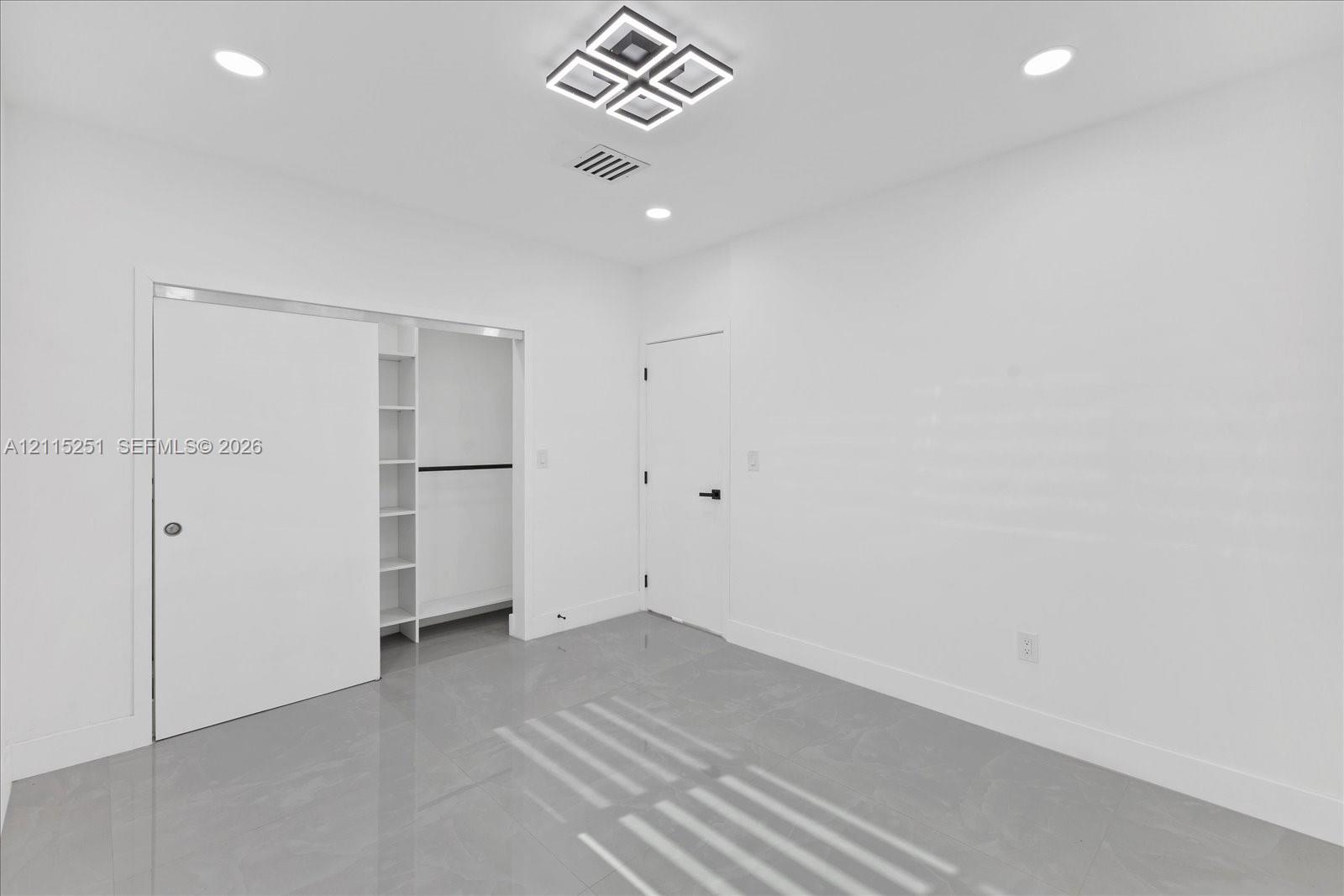 Neutral interior space featuring polished tile flooring, recessed lighting, a geometric flush-mount light fixture, and a built-in closet system with open shelving