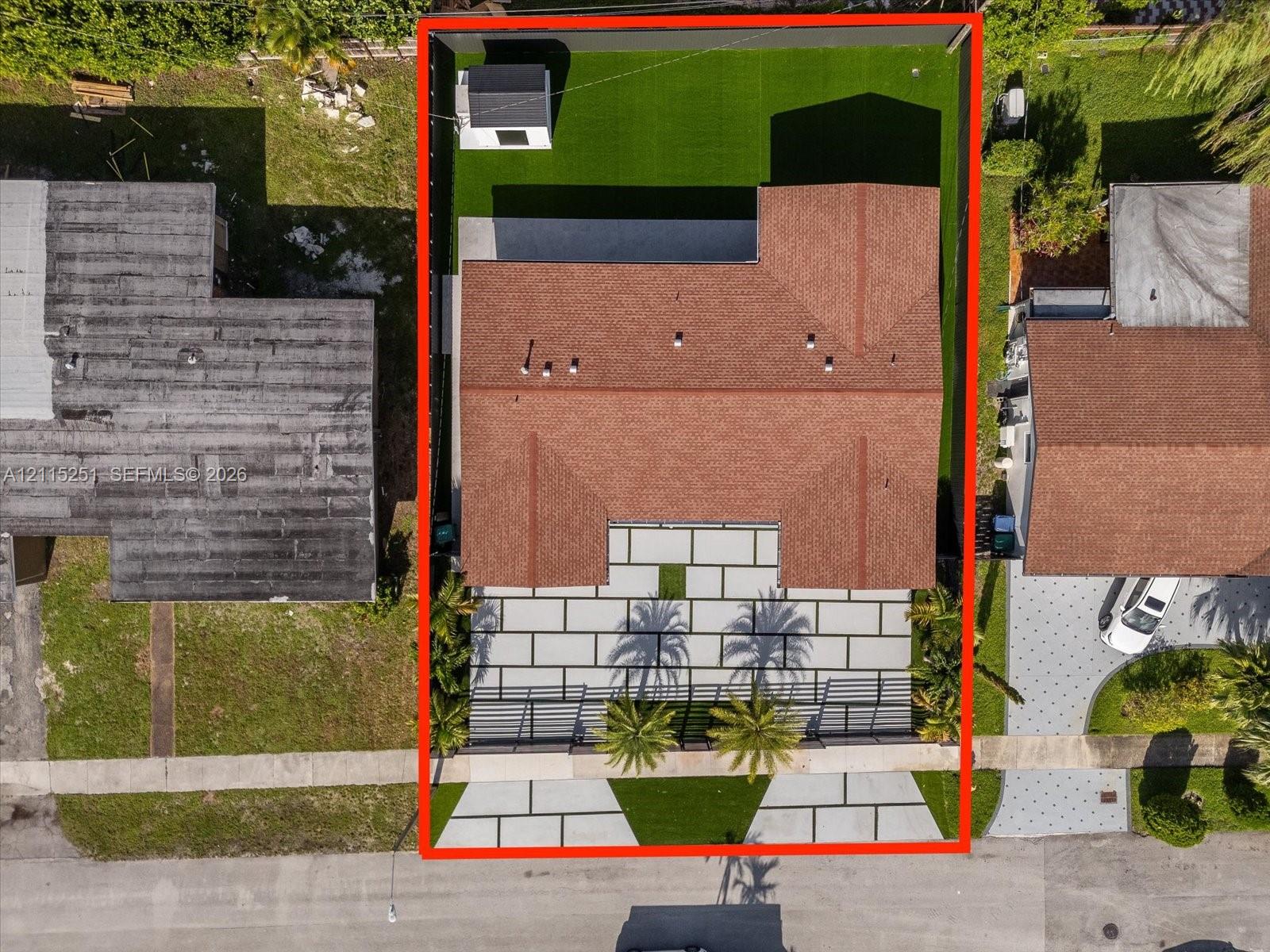 Aerial perspective featuring a structured, low-maintenance turf lawn, paved front hardscaping, and an enclosed backyard area with a dedicated storage structure