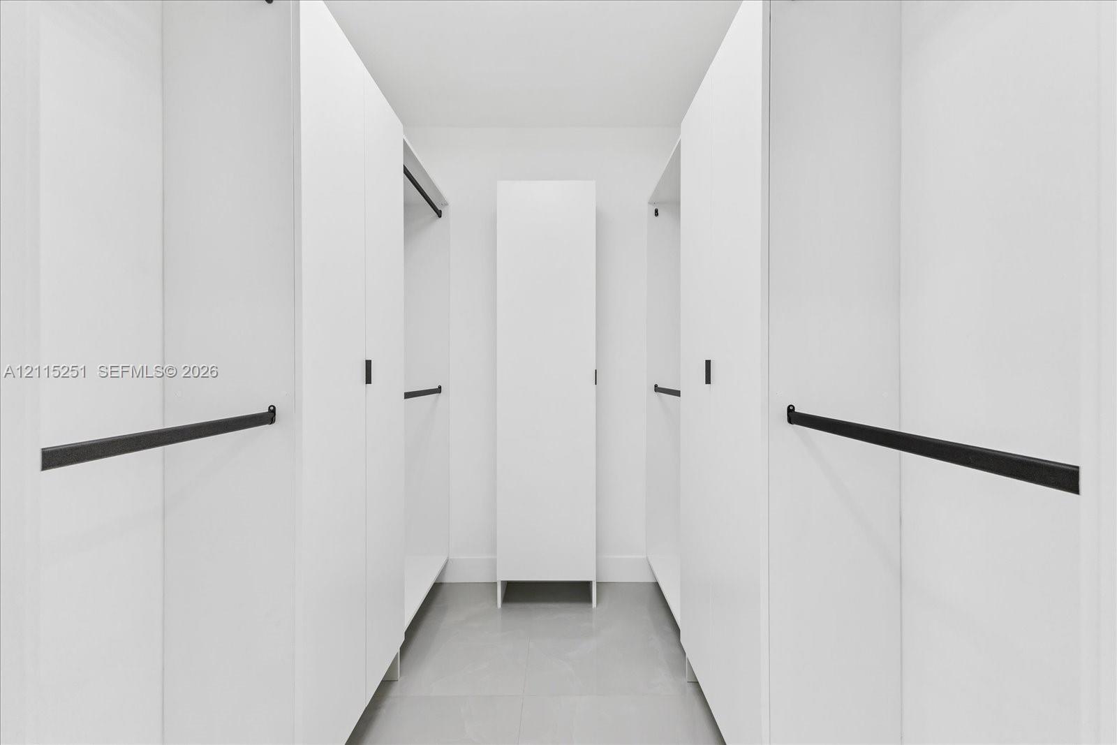 Custom storage organization featuring white cabinetry, matte black hardware, and integrated hanging rods, finished with tile flooring