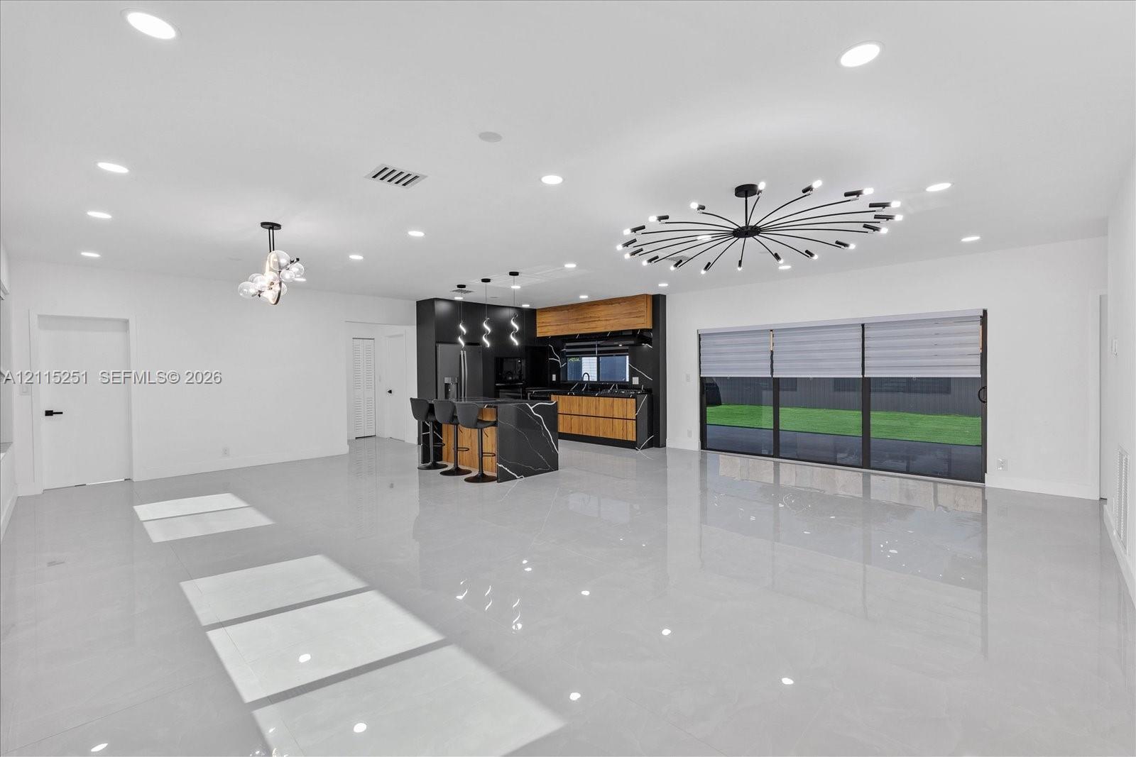 Open-concept interior featuring large-format tile flooring, recessed lighting, and a central kitchen island with high-contrast cabinetry