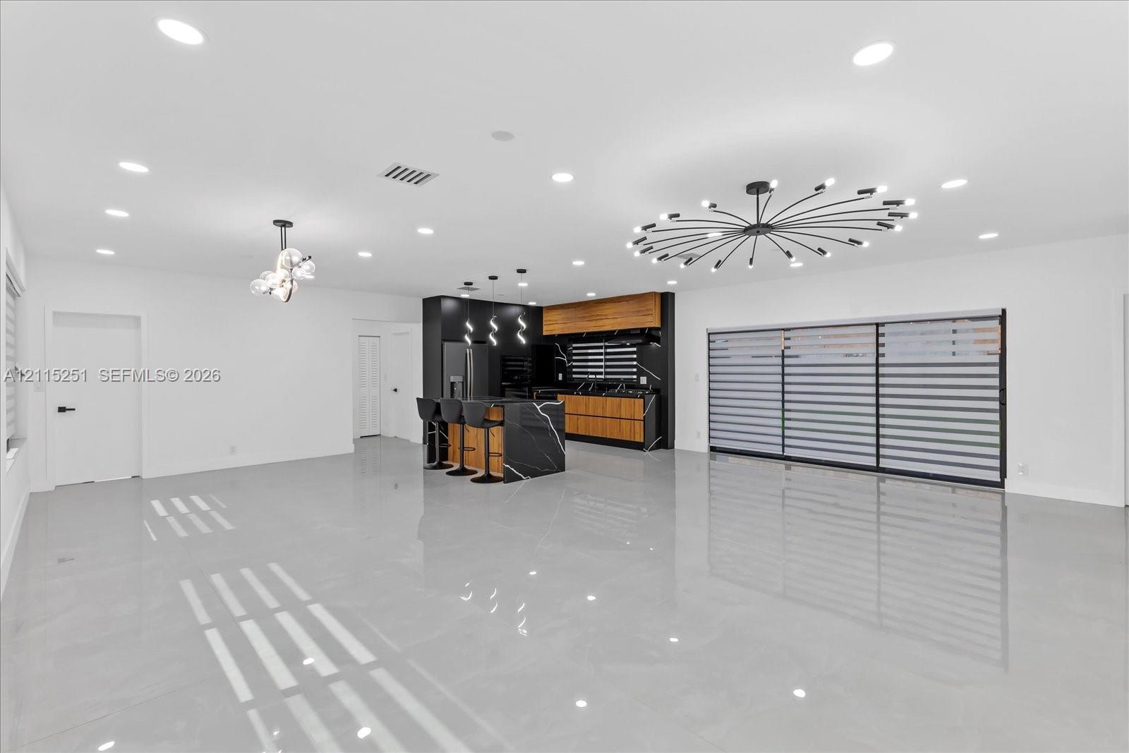 Open-concept kitchen featuring two-toned cabinetry, a stone-surface waterfall island, recessed lighting, and large-format tile flooring