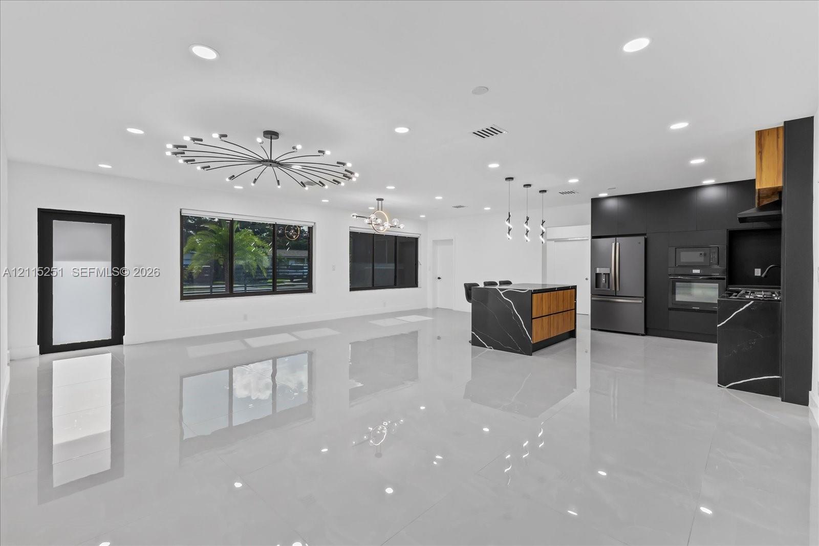 Open-concept living space featuring high-gloss tile flooring, recessed lighting, matte black cabinetry, and a kitchen island with stone-finish surfaces and wood-tone accents