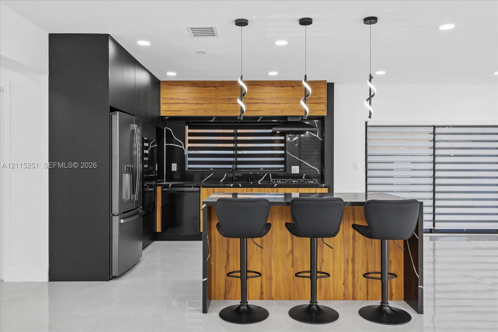 Kitchen featuring matte black cabinetry, wood-finish upper cabinets, a waterfall-edge island, stone-patterned backsplash, and modern pendant lighting