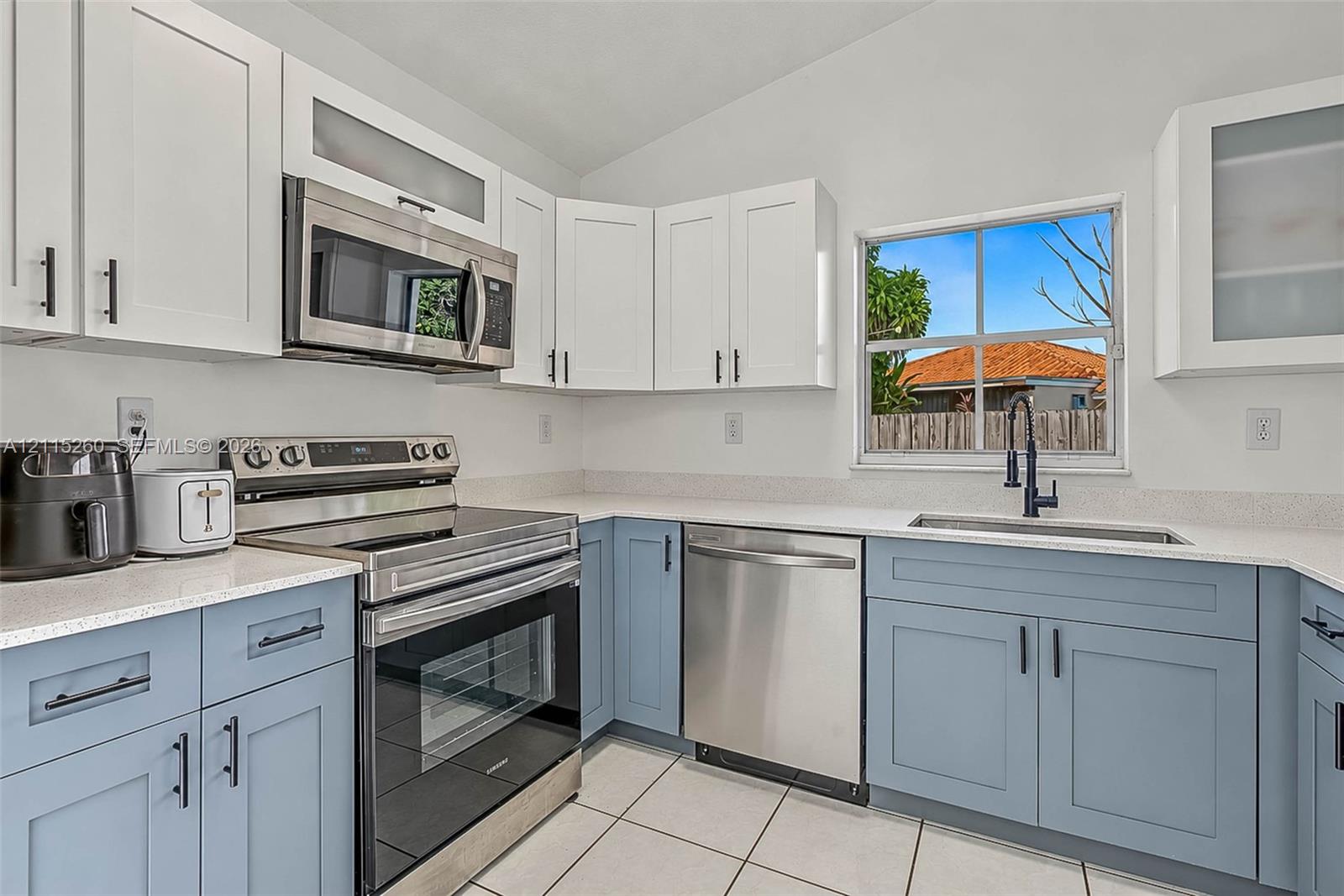 Two-toned cabinetry with upper white shaker-style cabinets and lower blue shaker-style cabinets, light-toned stone-finish countertops, stainless steel appliances, and a single-basin undermount sink with a matte black faucet
