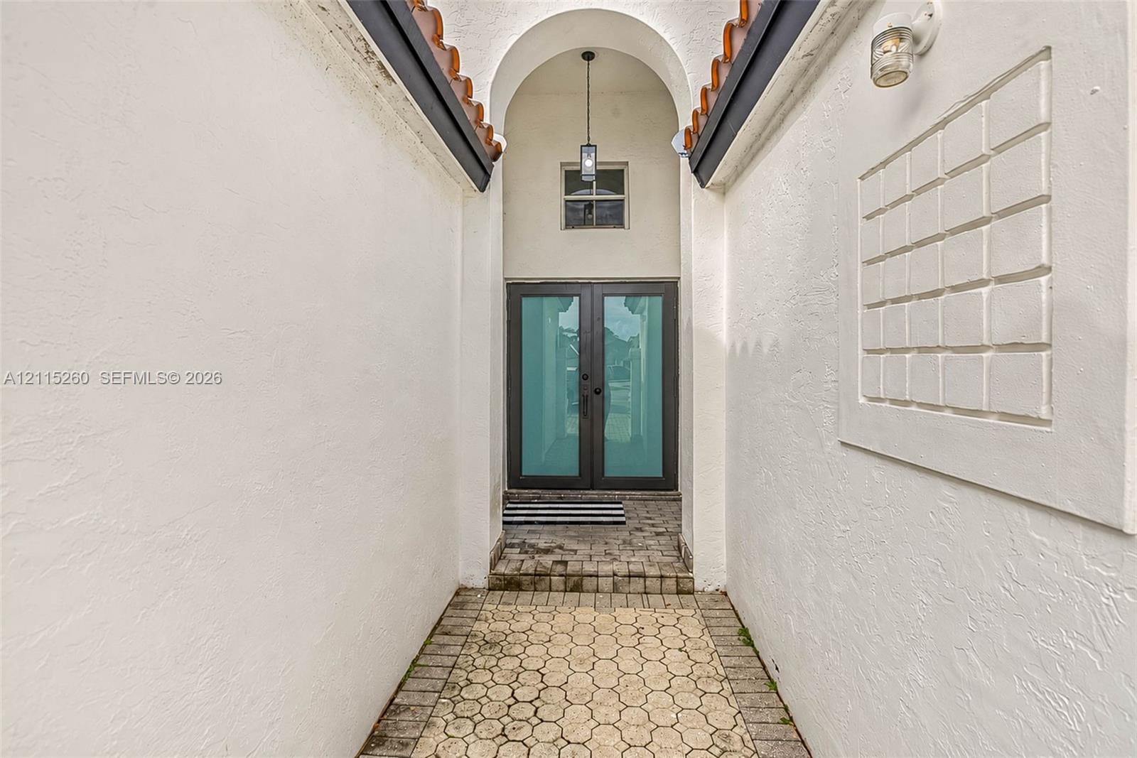 Entryway featuring a double-door entrance with glass panels, an arched ceiling with a pendant light, a recessed square wall relief, and paver stone flooring