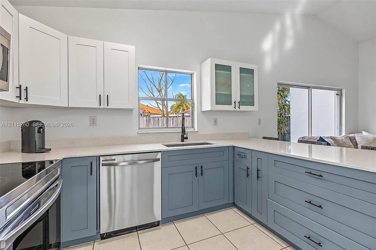 Kitchen featuring two-tone cabinetry with matte black hardware, stone-composite countertops, stainless steel dishwasher, glass-front upper cabinets, and tile flooring
