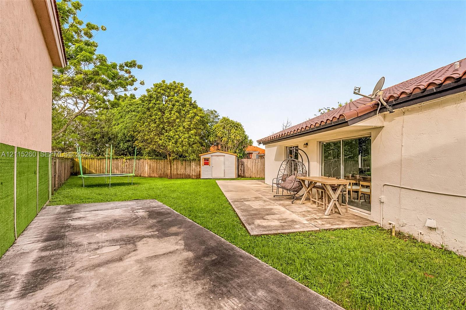 Backyard featuring a concrete patio, grassy lawn, wood privacy fencing, and a detached storage shed
