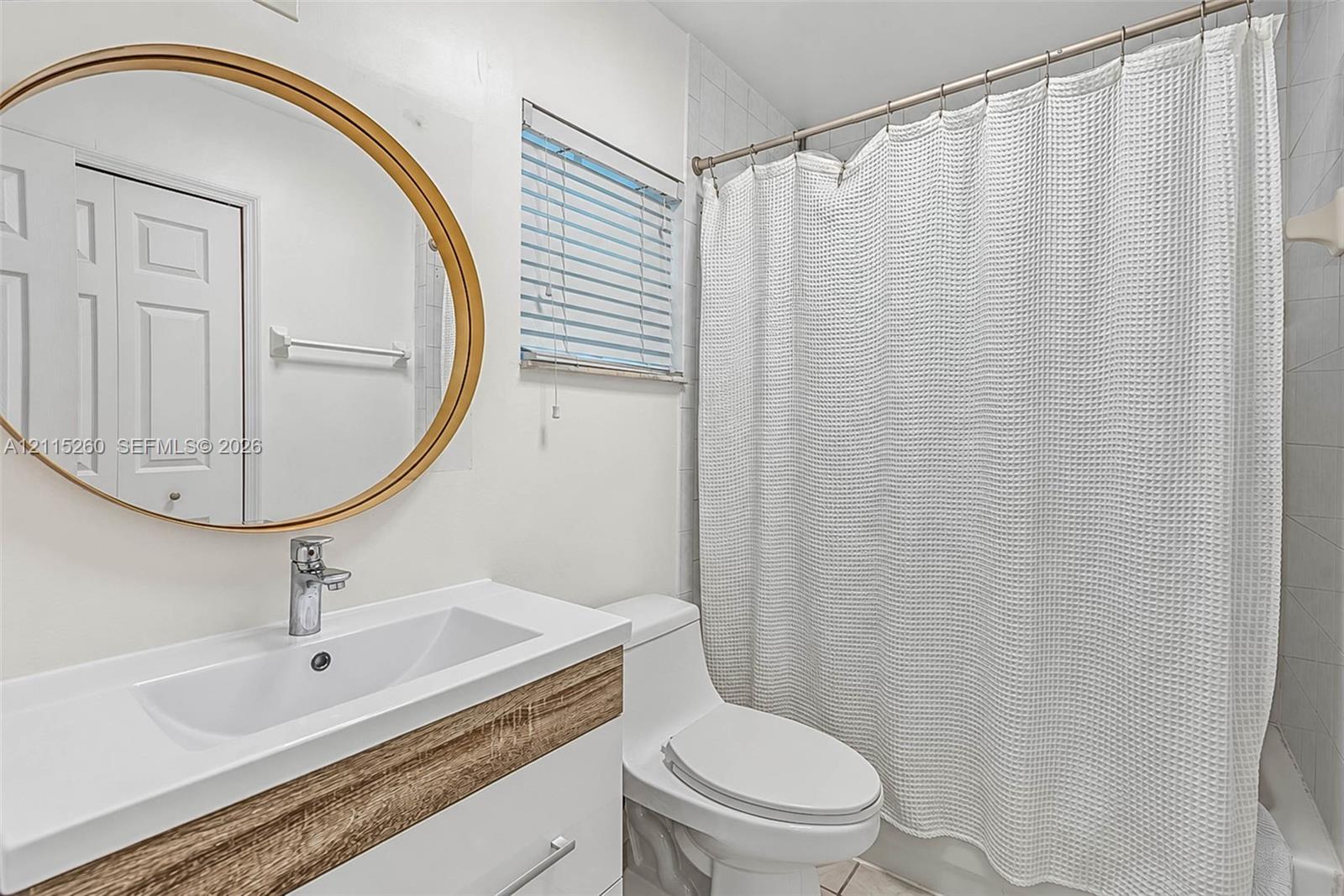 Bathroom featuring a white vanity with wood-finish detailing, integrated rectangular sink, round mirror with a metallic frame, and a tub-shower combination with tile surround
