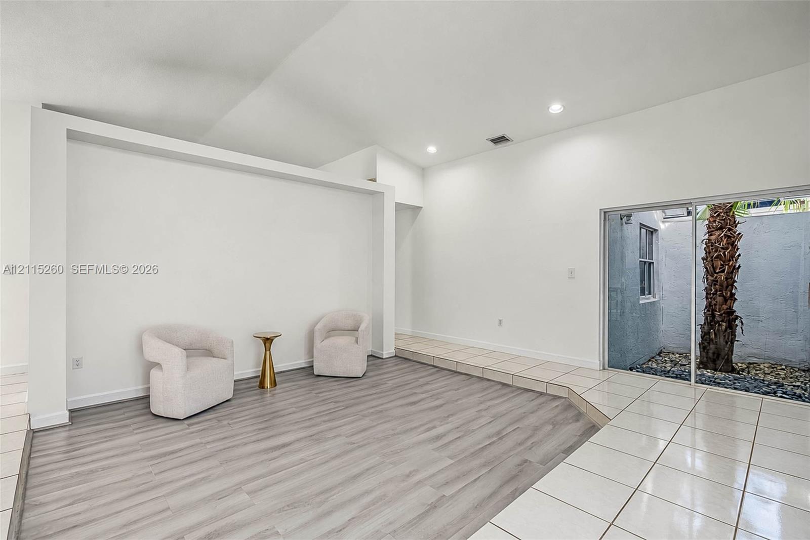 Interior featuring vaulted ceilings, wood-finish flooring, recessed lighting, and a sliding glass door providing external access to a walled courtyard