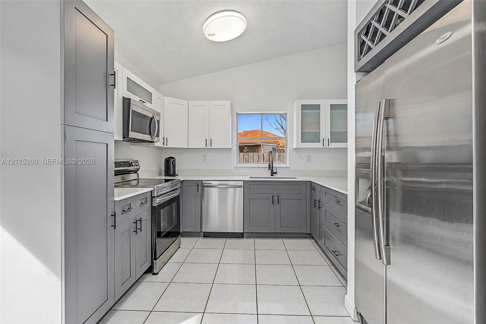 Kitchen featuring two-tone shaker cabinetry, solid-surface countertops, stainless steel appliances, ceramic tile flooring, and integrated wine storage
