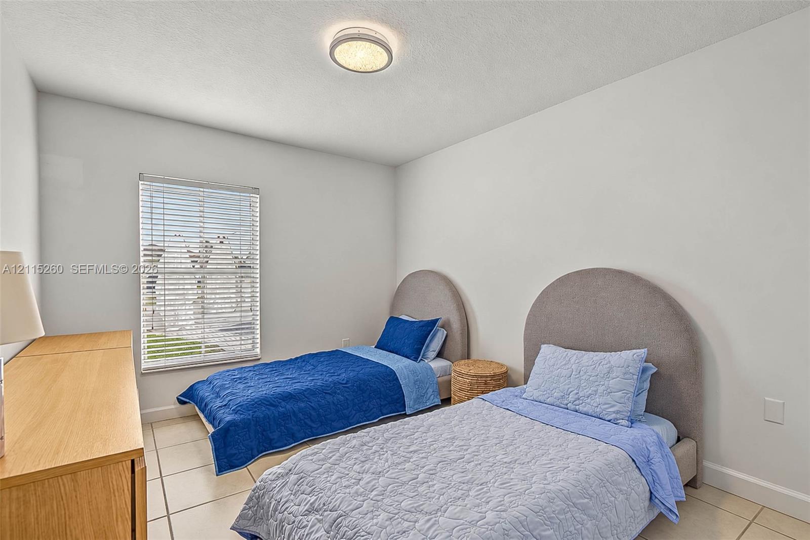 Neutral-toned interior room featuring large-format ceramic tile flooring, a flush-mount circular ceiling light fixture, and a window with horizontal blinds