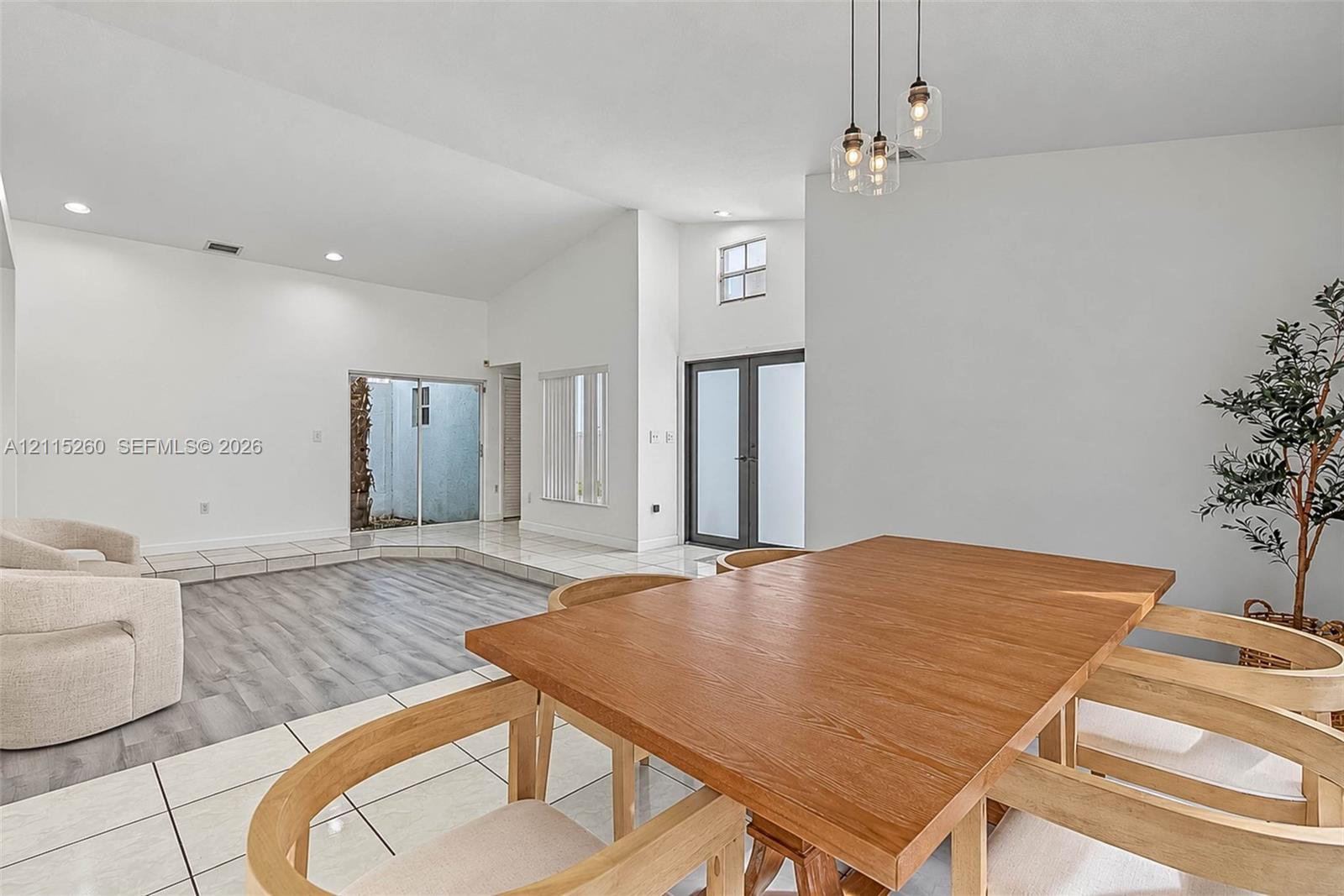 Vaulted ceilings with recessed lighting, wood-finish flooring, large-format tile flooring, multi-pane glass entry doors, and triple-pendant glass lighting fixtures