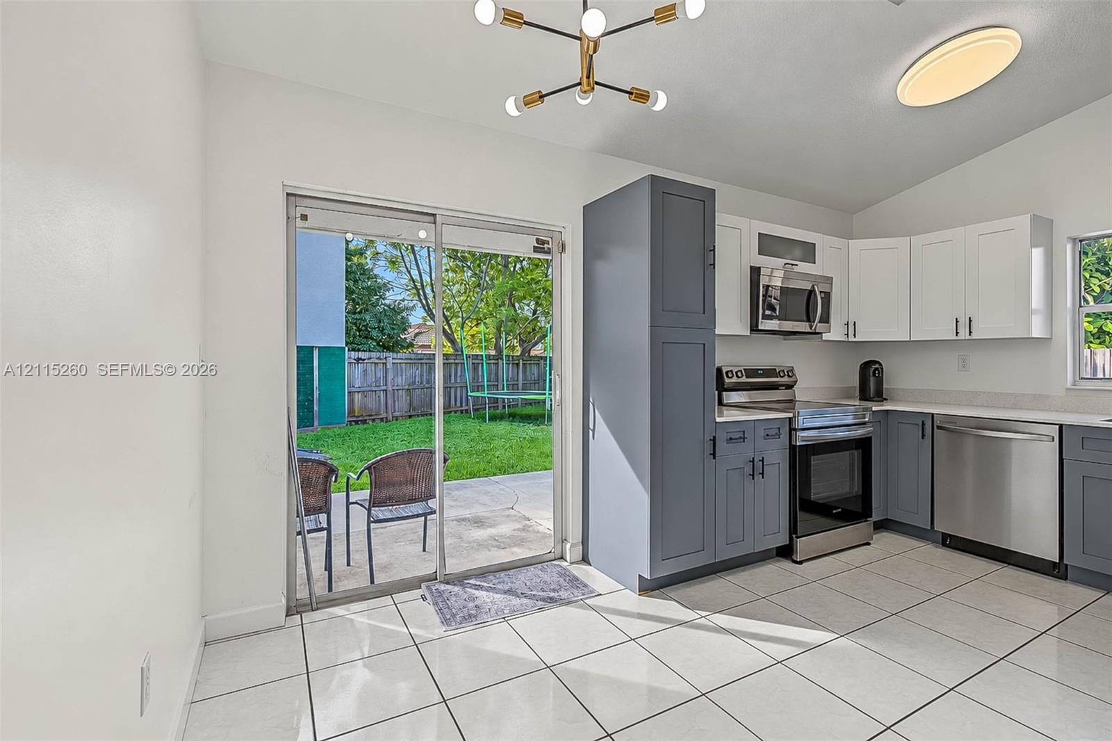 Kitchen featuring two-tone cabinetry, stainless steel appliances, white tile flooring, a multi-arm geometric light fixture, and a sliding glass door