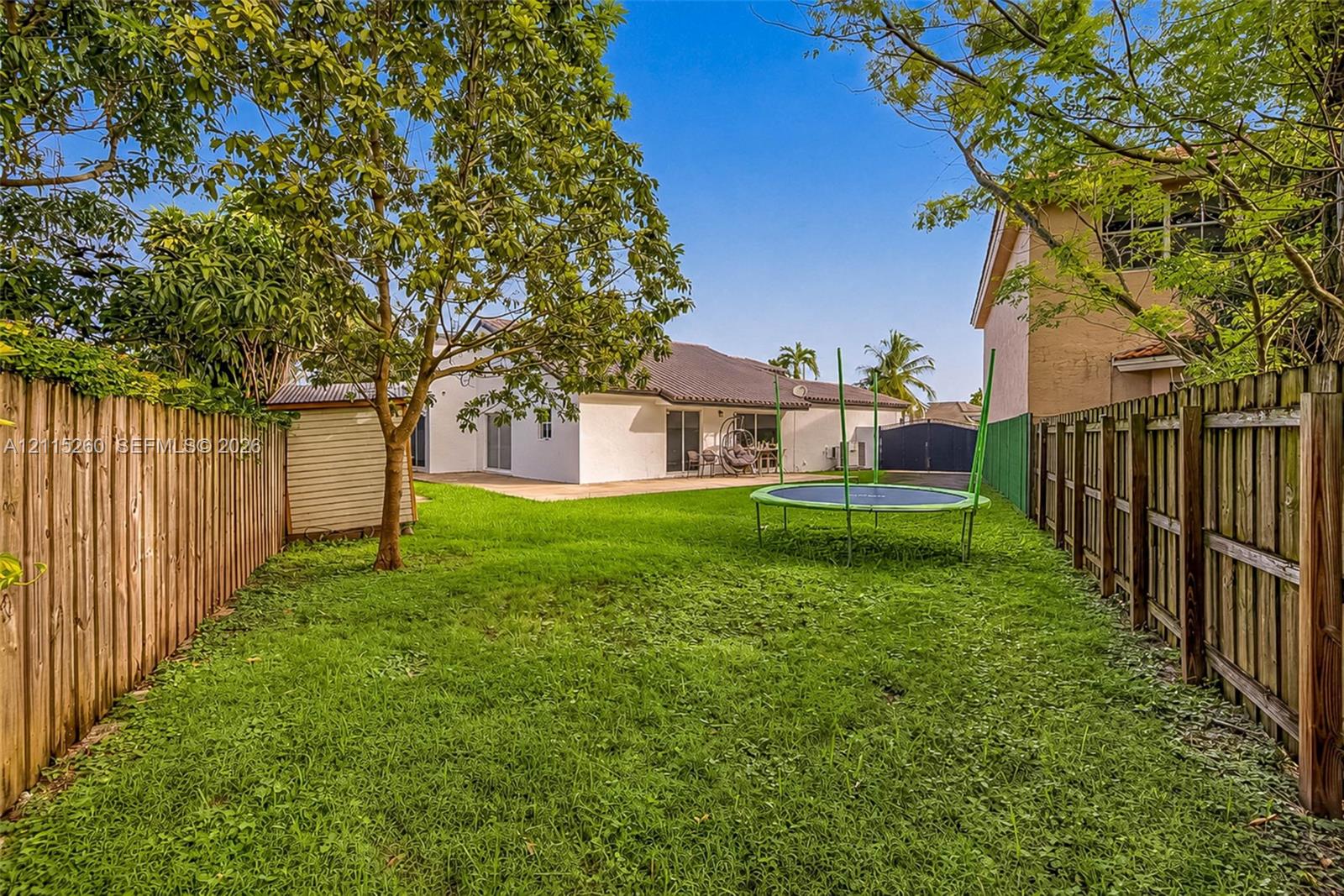 Expansive backyard featuring a fenced perimeter, manicured lawn, and mature trees