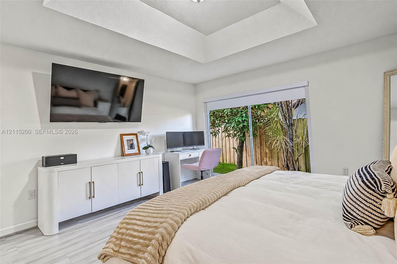 Tray ceiling, light-toned wood-finish flooring, white built-in cabinetry with metal pulls, and sliding glass doors