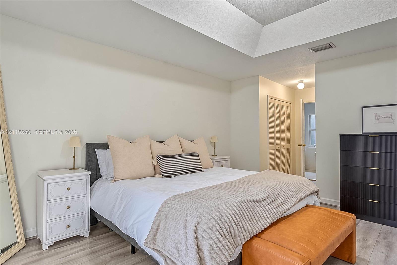 Tray ceiling featuring crisp white paint, louvered bi-fold closet doors, and wood-finish flooring