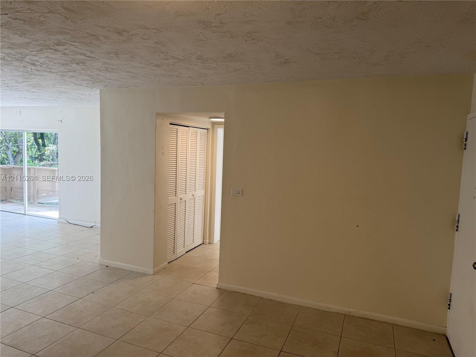 Neutral-toned interior space featuring large-format tile flooring, textured ceiling finish, and a closet with white louvered doors