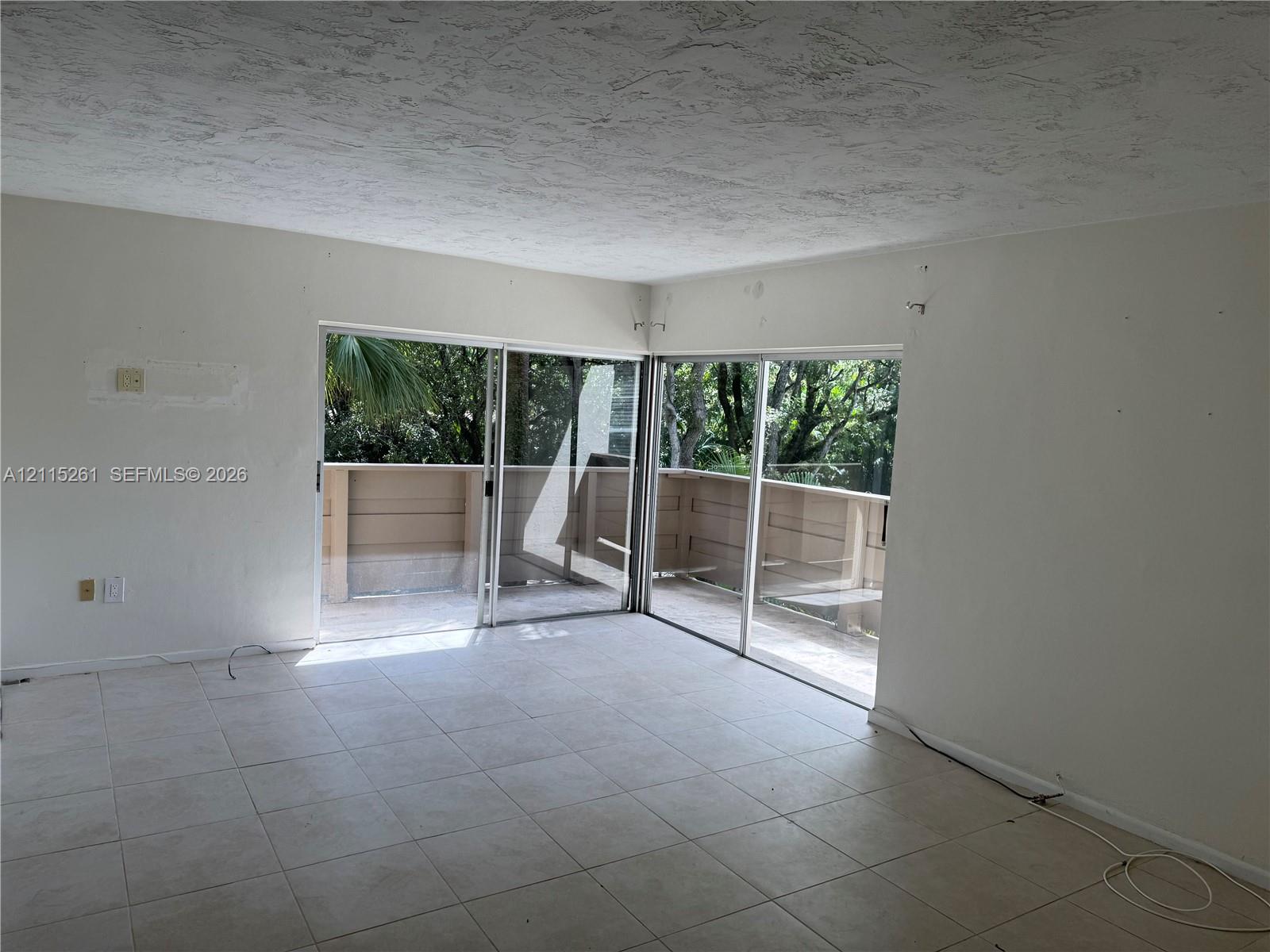 Interior space featuring ceramic tile flooring, neutral wall finishes, and dual glass sliding doors opening to a wrap-around balcony with solid privacy railing