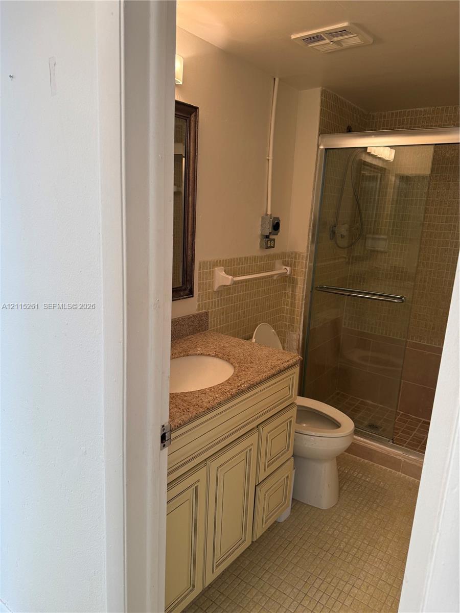Bathroom featuring a stone-top vanity with an integrated basin, a walk-in shower with a glass enclosure, and tiled wall and floor surfaces
