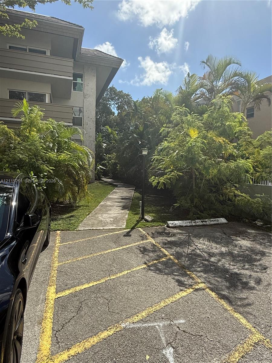 Multi-story building exterior featuring concrete walkways, paved parking area with marked stalls, and mature landscaping