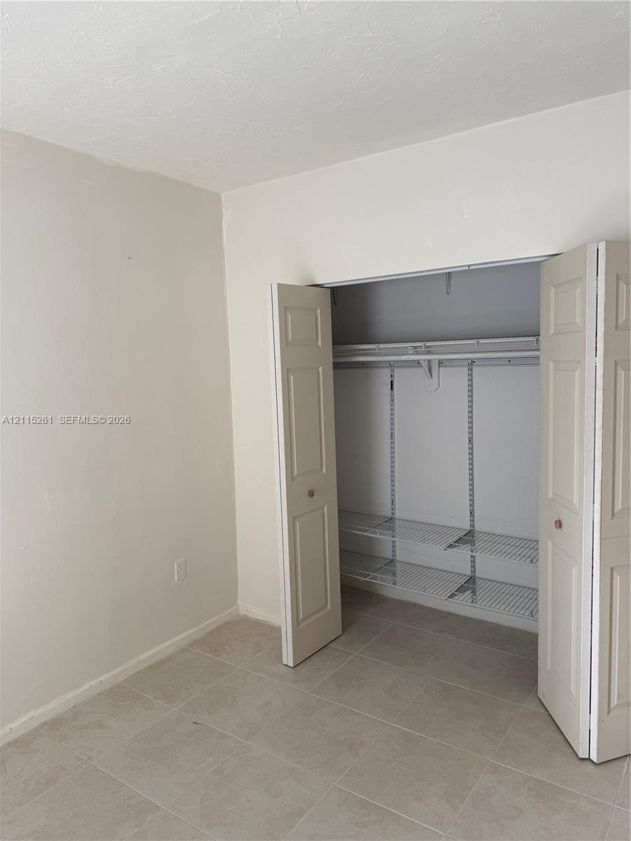 Neutral-toned interior space featuring light-colored tile flooring and a built-in closet with paneled bifold doors, an integrated hanging rod, and adjustable wire shelving