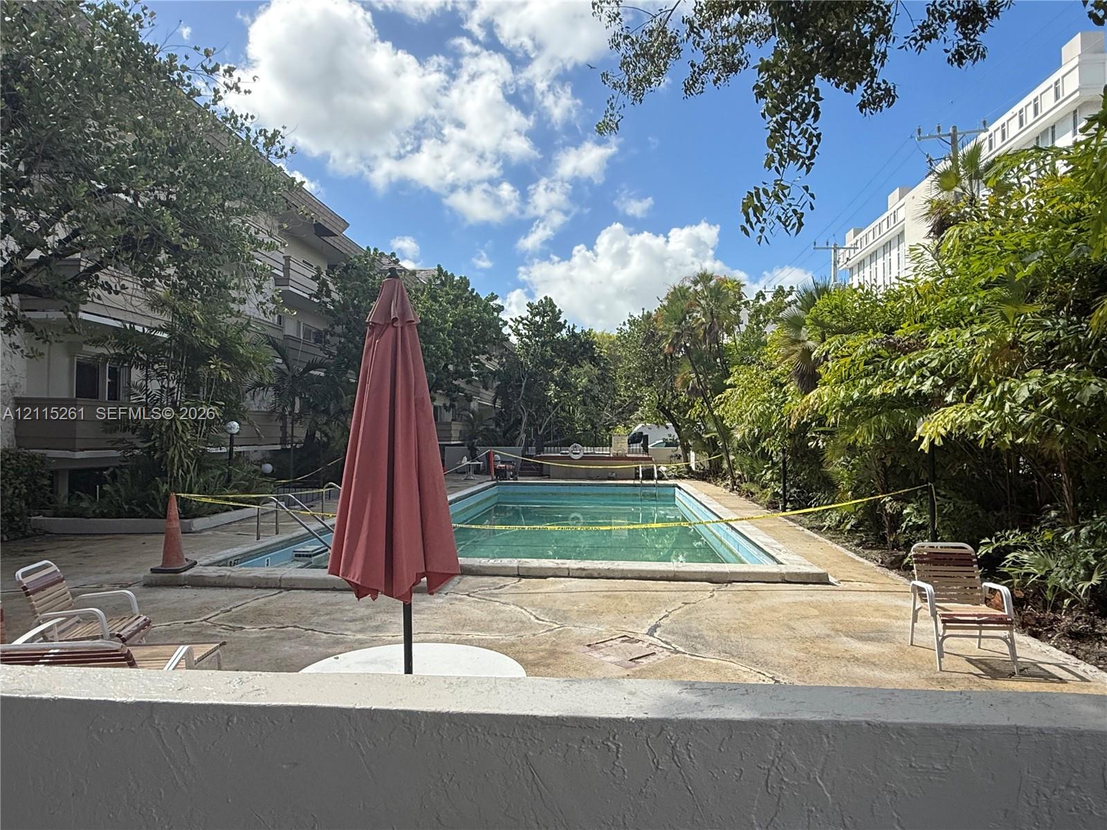 In-ground swimming pool surrounded by a concrete patio, landscaped greenery, and mature trees