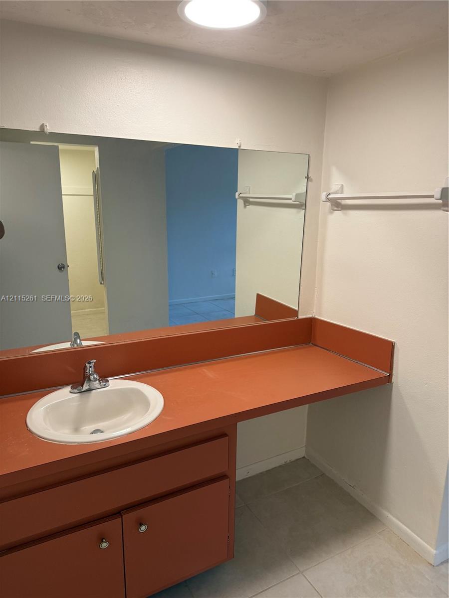 Bathroom vanity featuring an integrated countertop with a drop-in sink, chrome faucet, expansive wall-mounted mirror, and tile flooring