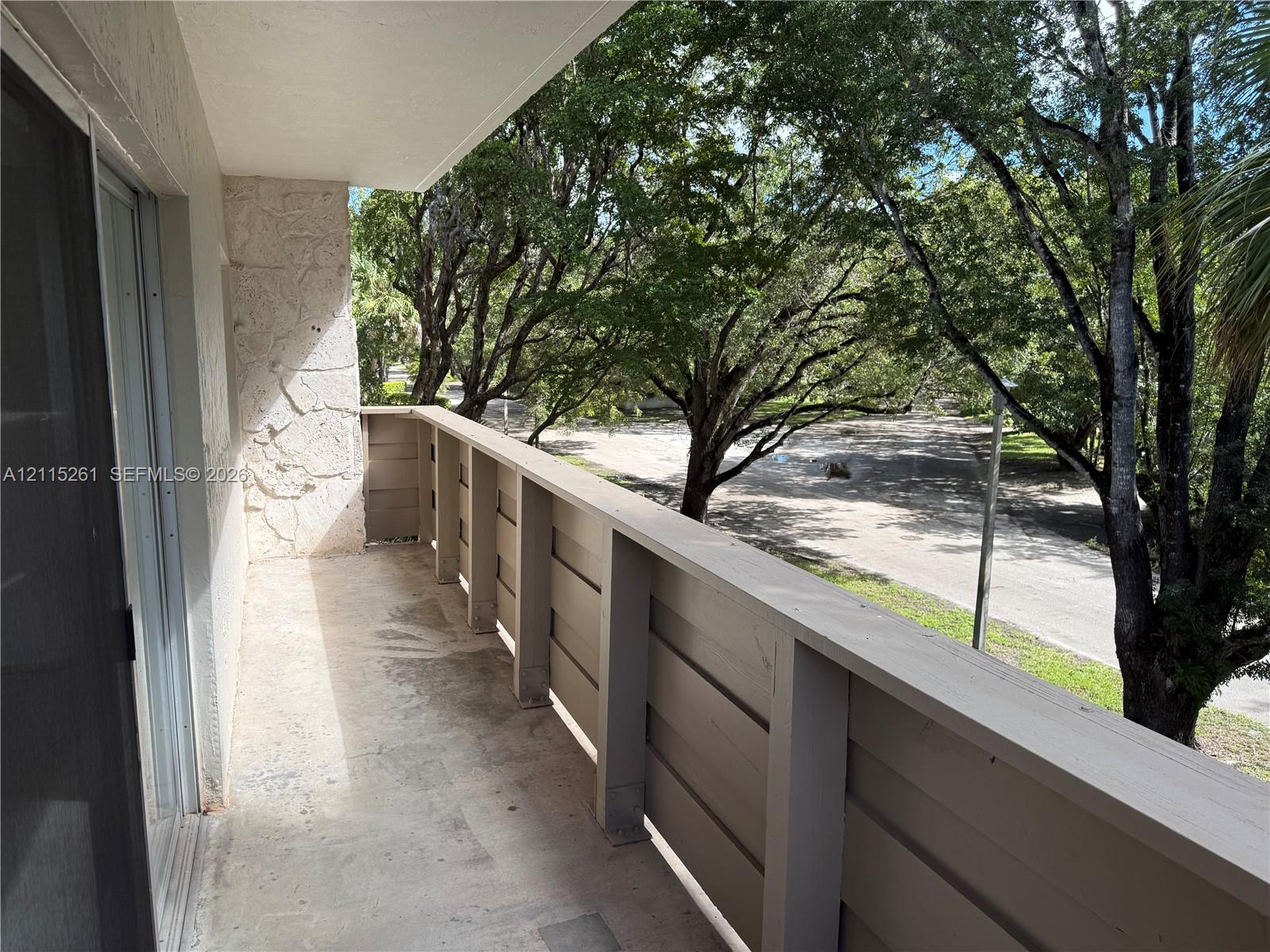 Private balcony featuring a concrete floor, horizontal wood-style railing, and natural stone wall accents, framed by mature trees