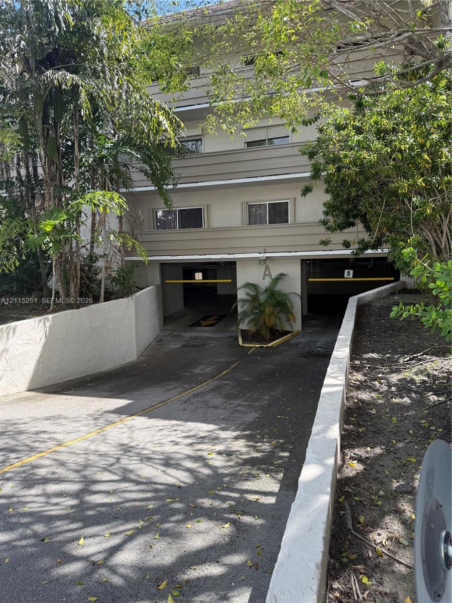 Multi-level residential exterior featuring a covered parking garage with two access bays, concrete retaining walls, and established tropical landscaping